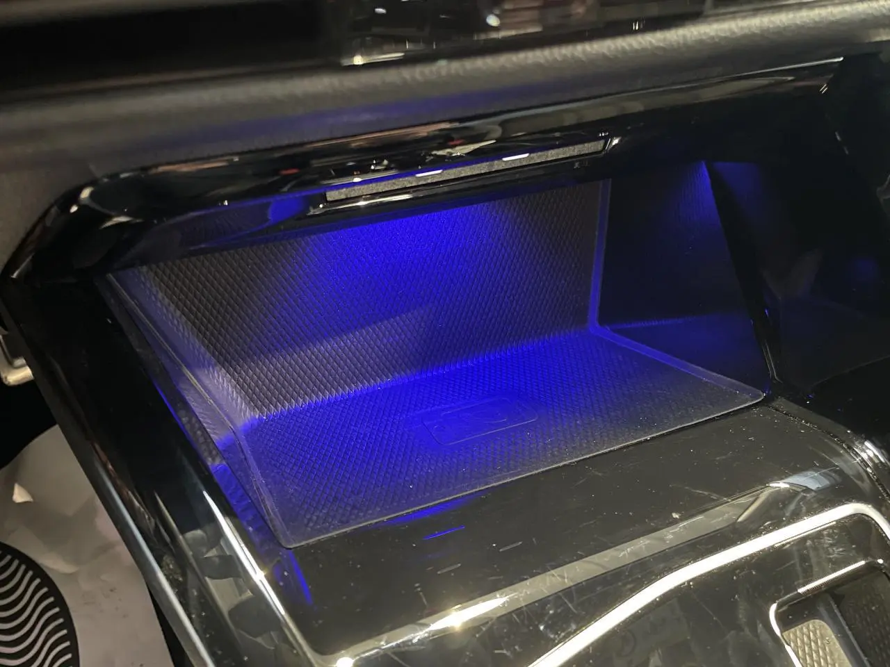 Gros plan sur le compartiment de recharge sans fil avec éclairage d'ambiance bleu dans une Volkswagen Golf VIII R-Line noire.
