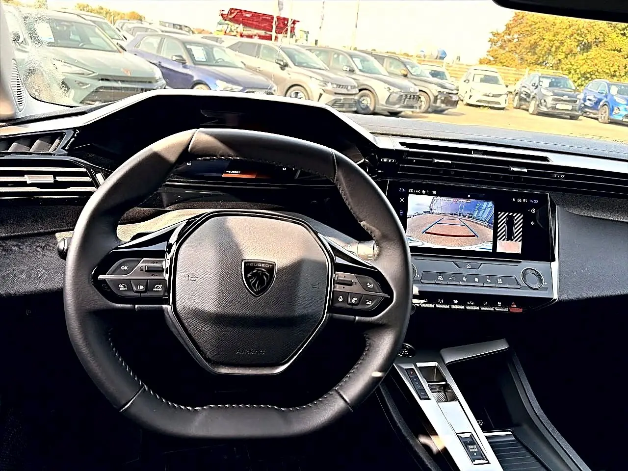 Vue intérieure centrée sur le volant Peugeot noir et l'écran tactile affichant la caméra de recul.