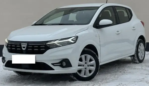 Vue 3/4 avant droite d'une Dacia Sandero 2023 blanc glacier avec calandre noire et feux LED allumés sur sol enneigé.