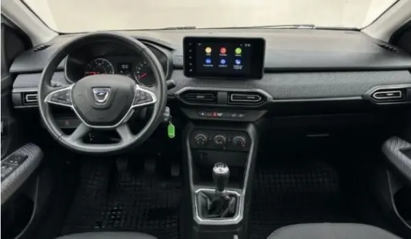 Vue intérieure frontale du tableau de bord noir de la Dacia Sandero 2023 avec écran tactile et levier de vitesse manuel.