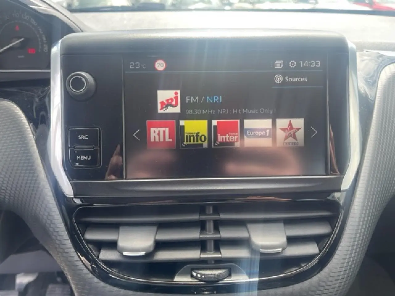 Vue rapprochée de l’écran tactile central de la Peugeot 208 blanc perle, affichant les stations radio avec commandes autour.