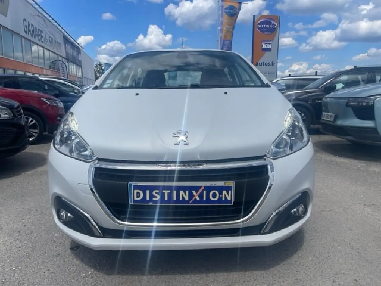 Vue frontale d'une Peugeot 208 blanche perle avec calandre chromée et logo lion bien visible au centre.