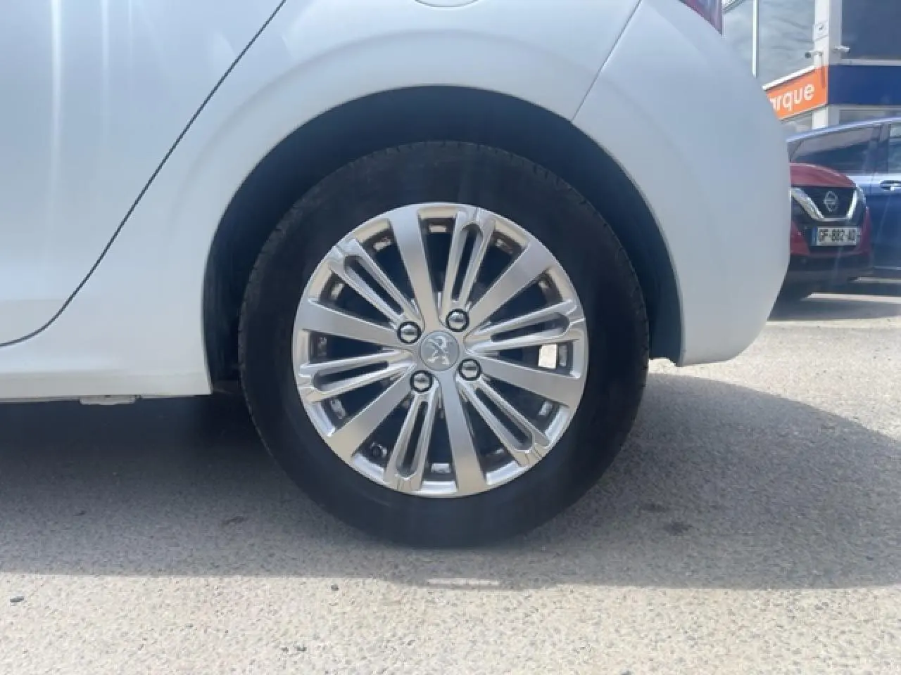 Gros plan sur la roue arrière droite avec jante alliage 16' Titane Technical Grey d'une Peugeot 208 blanc perle texture.