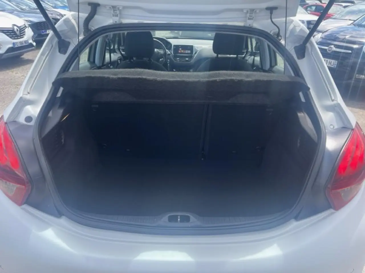 Coffre ouvert vu de l'arrière d'une Peugeot 208 blanc perle, avec intérieur sombre et banquette arrière visible.