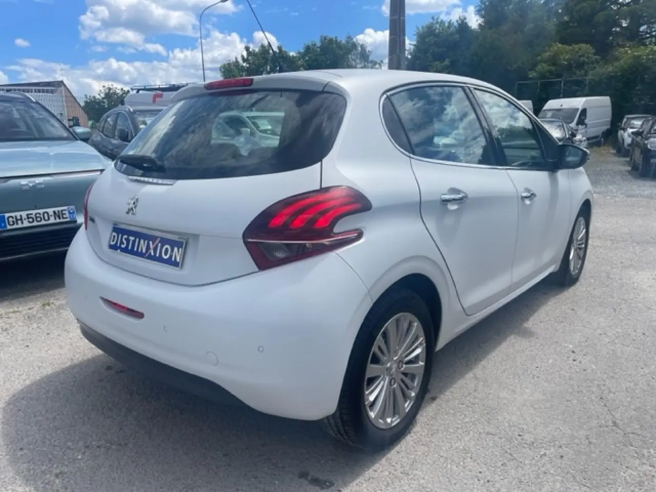 Vue 3/4 arrière droite d'une Peugeot 208 blanche perle avec jantes alliage et feux arrière distinctifs.