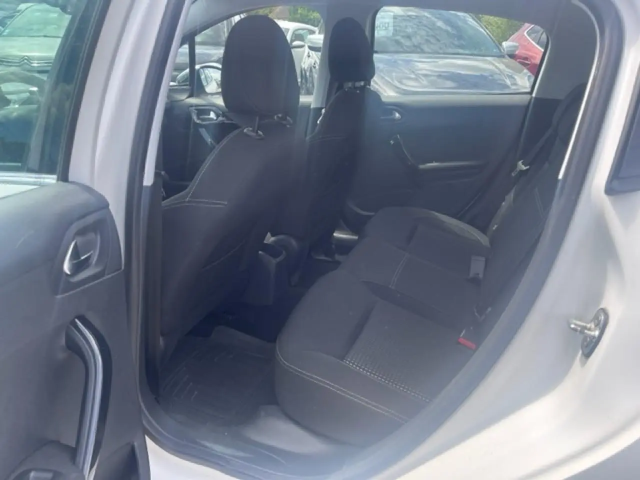Vue intérieure côté arrière droit de la Peugeot 208 blanche perle, montrant les sièges arrière noirs et les portes ouvertes.