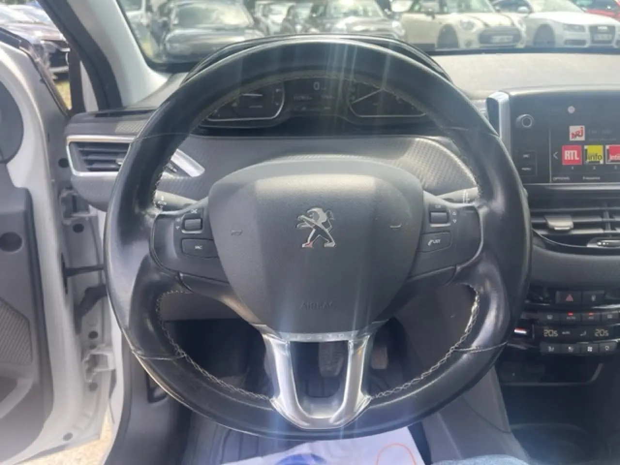 Vue intérieure centrée sur le volant cuir multifonction d'une Peugeot 208 blanc perle, avec tableau de bord et écran tactile visibles.
