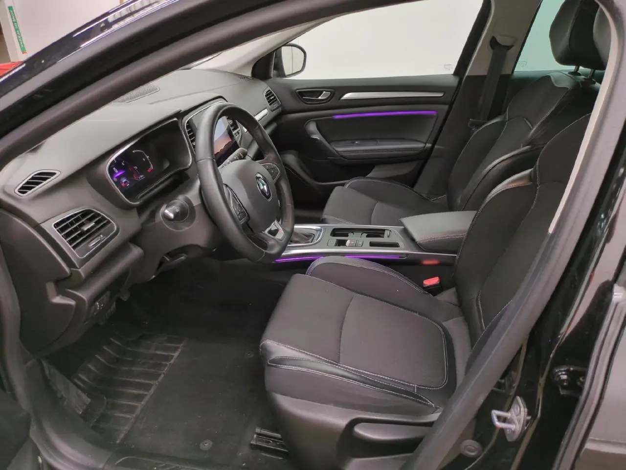 Intérieur avant droit de la Renault Mégane noire, avec sièges tissu noir et éclairage d'ambiance violet sur la porte et console.