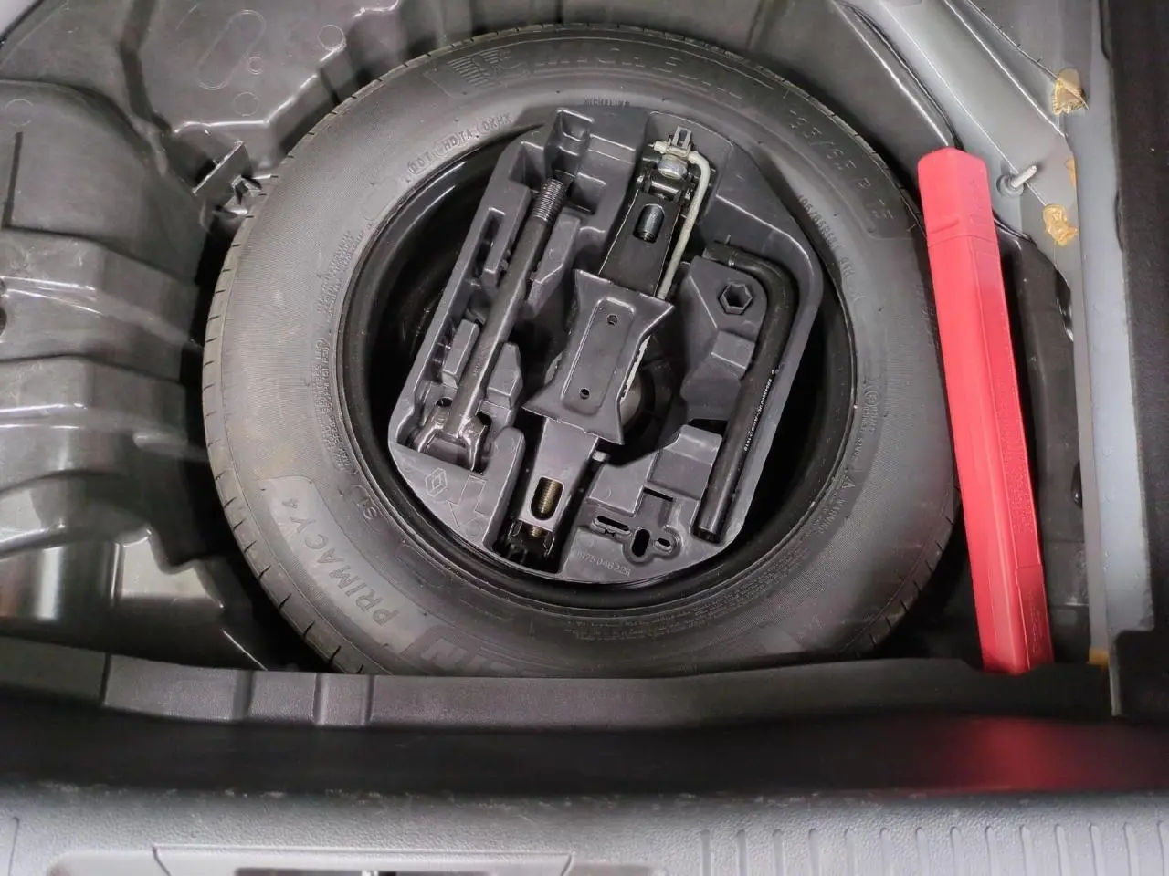 Vue plongeante sur la roue de secours noire et son kit d'outils dans le coffre de la Renault Mégane noir métal 2023.