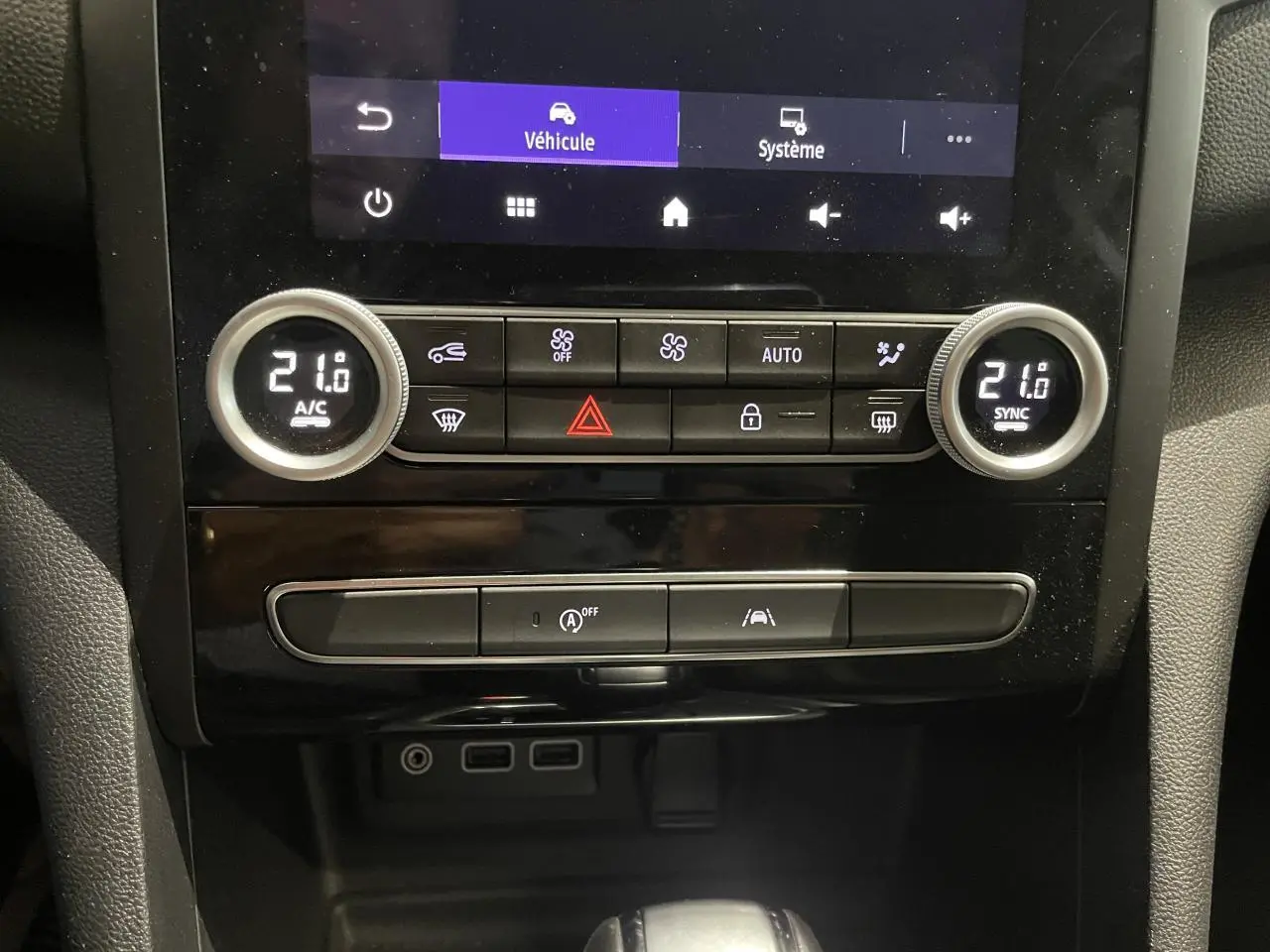 Vue rapprochée de la console centrale de la Renault Mégane noire, avec commandes climatisation bi-zone et prises USB visibles.
