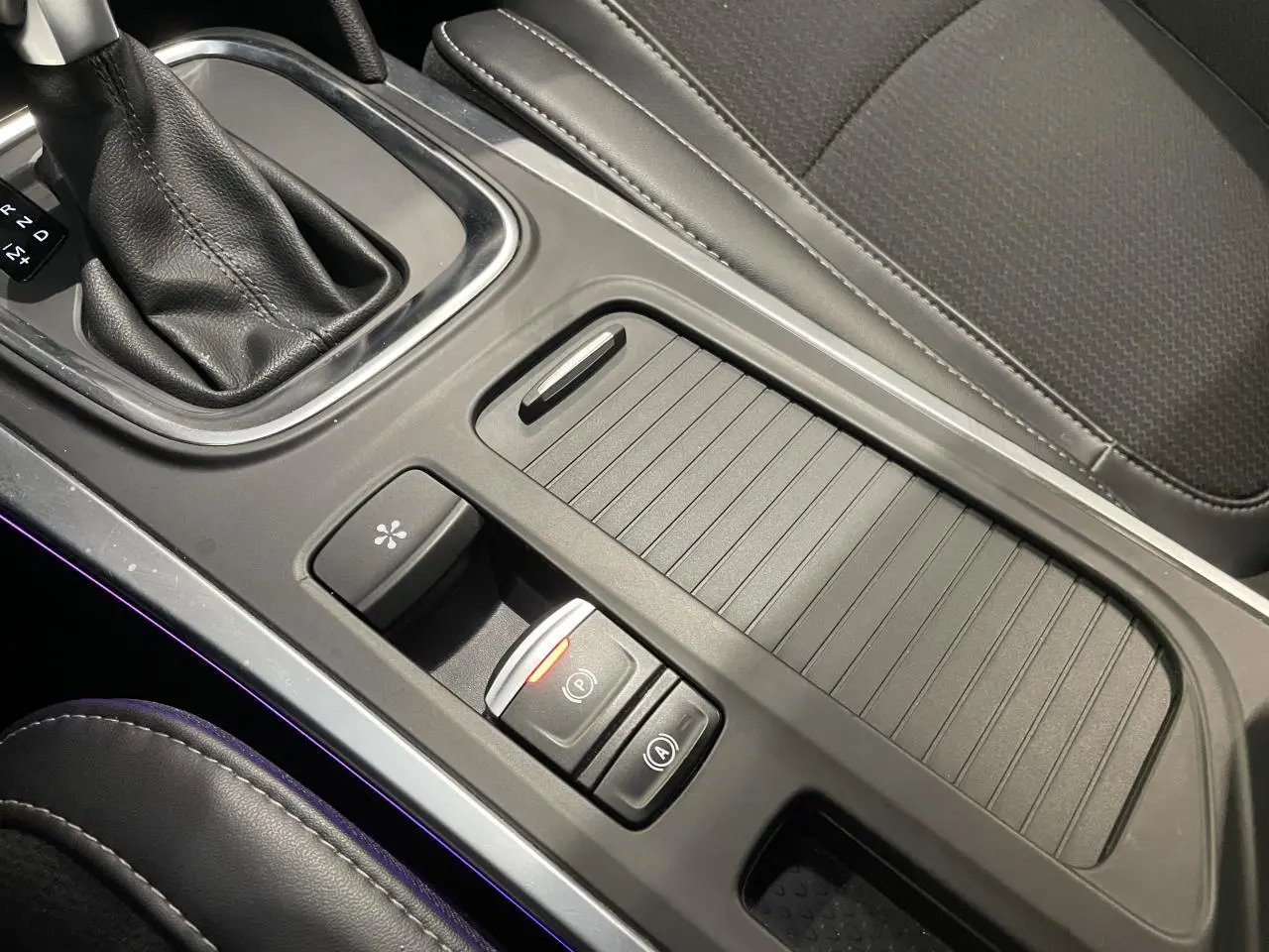 Vue rapprochée de la console centrale noire avec frein de parking électrique et sellerie tissu gris de la Renault Mégane 2023.