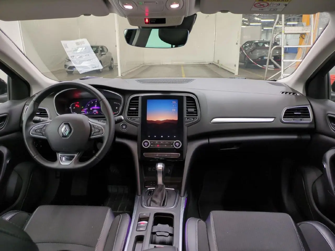 Vue intérieure avant de la Renault Mégane 2023, tableau de bord noir avec écran tactile vertical et volant multifonction.