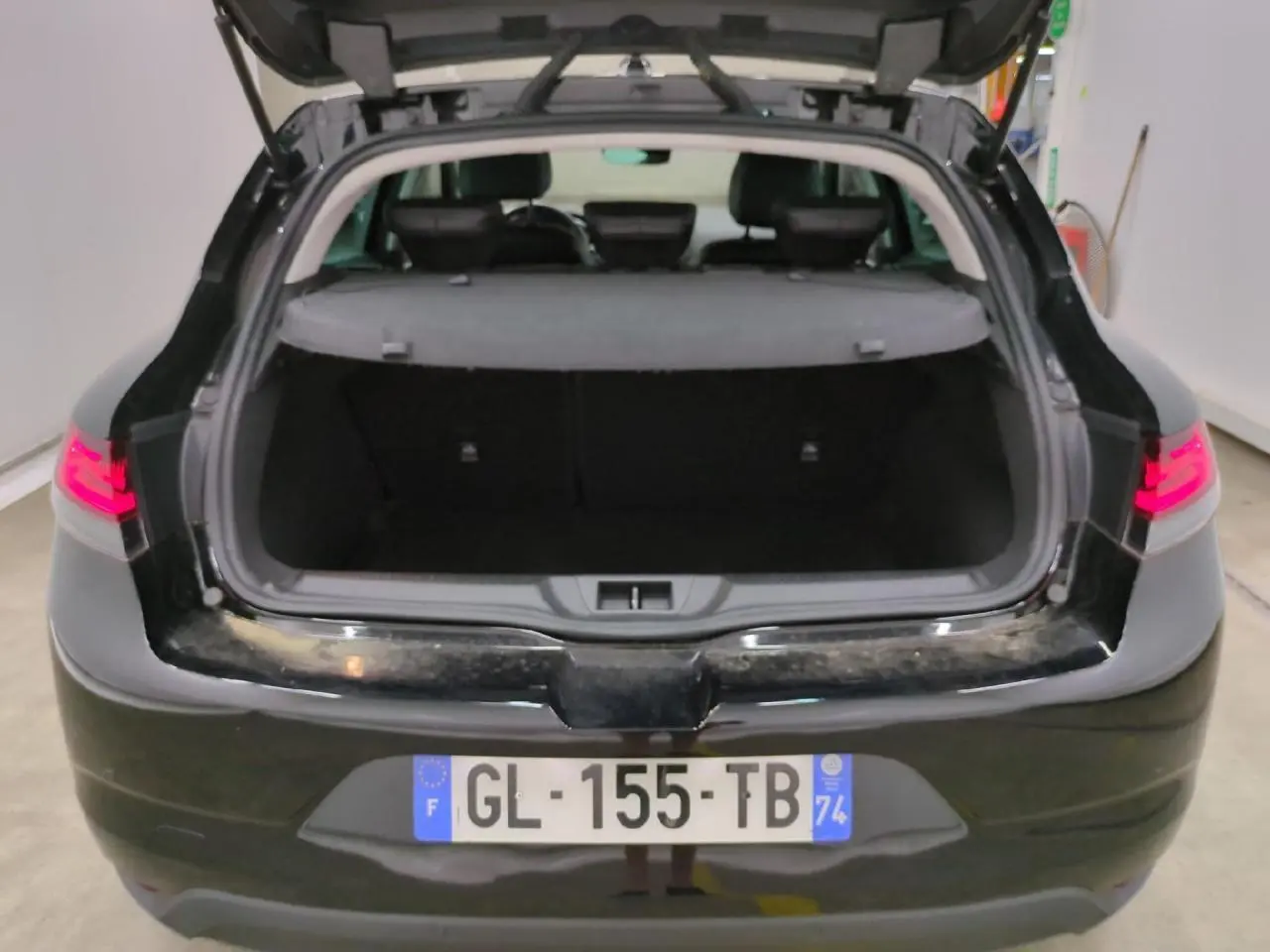 Vue arrière ouverte de la Renault Mégane noire métal 2023, coffre spacieux et feux arrière LED allumés.