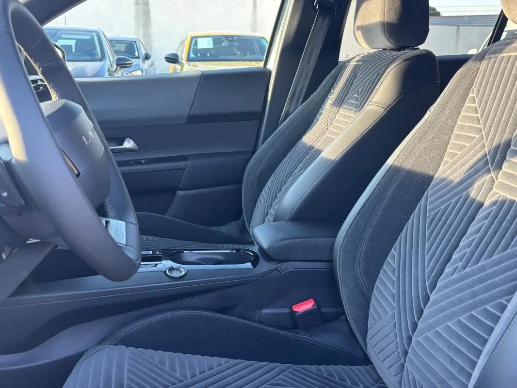 Vue intérieure côté conducteur de la Lancia Ypsilon 2025, sièges en tissu gris avec motifs géométriques et volant sport.
