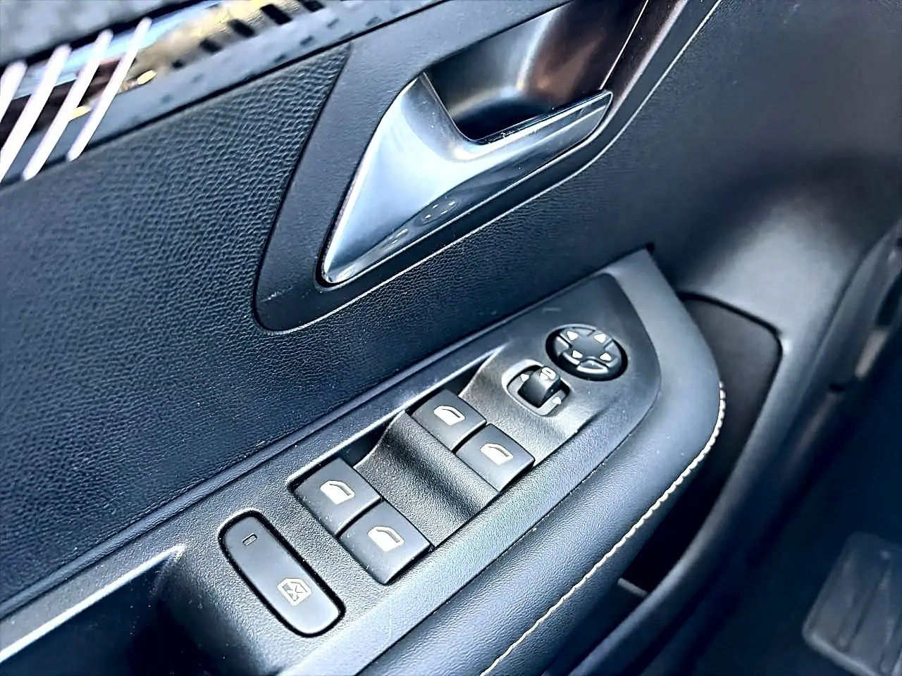 Gros plan sur la commande des vitres électriques côté gauche d’une Peugeot 208 gris selenium, intérieur noir.
