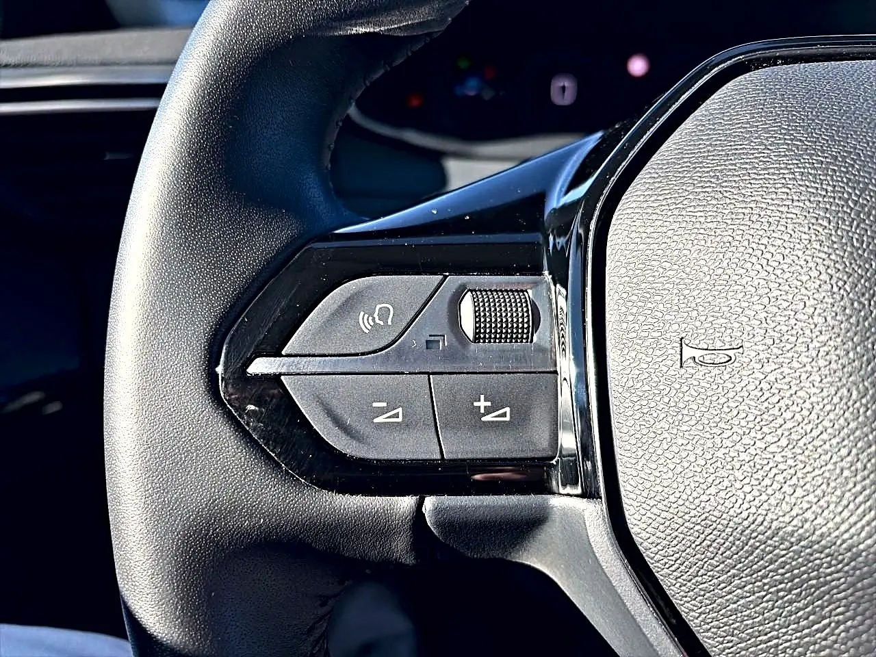 Gros plan sur les commandes gauche du volant noir de la Peugeot 208 1.2 100 Allure gris selenium, boutons de volume et appel mains-libres.