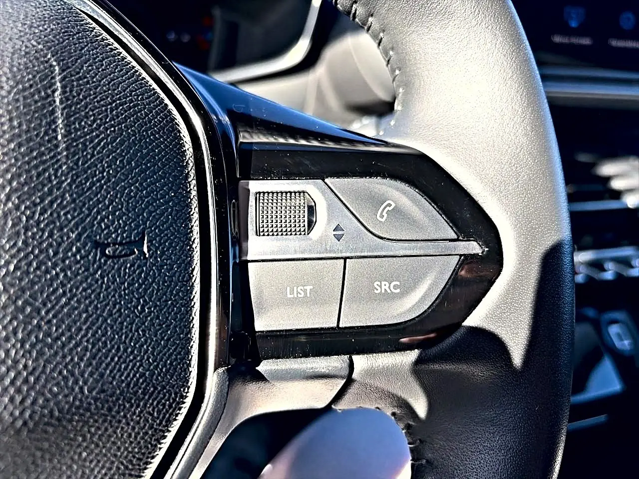 Gros plan sur les commandes audio au volant noir du Peugeot 208 1.2 100 Allure, intérieur lumineux.