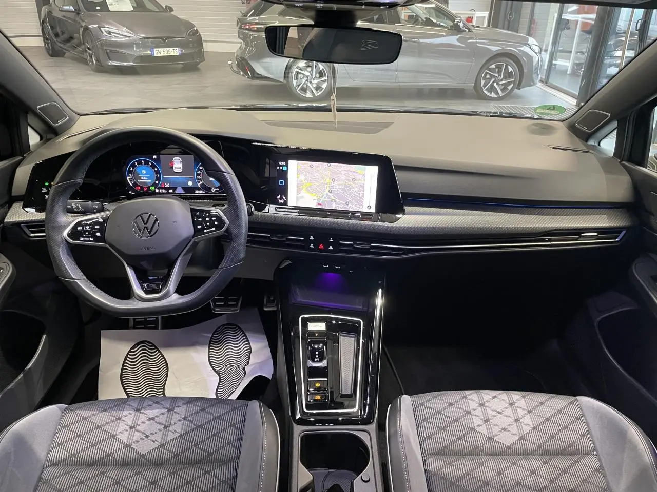 Vue intérieure avant de la Volkswagen Golf 1.5 eTSI 2024, tableau de bord noir avec écran tactile et volant multifonctions cuir.