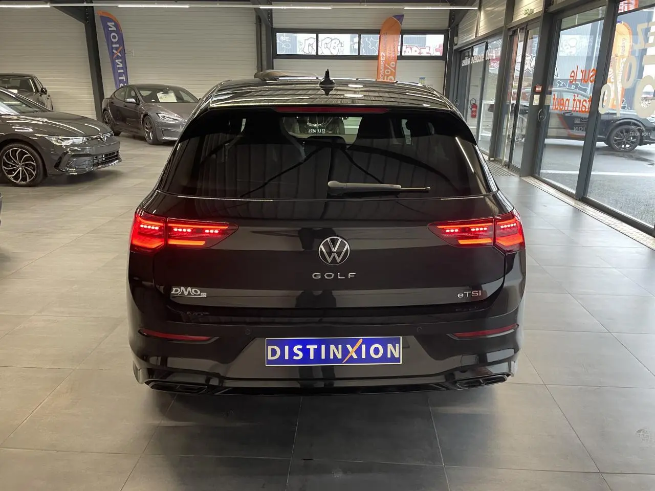 Vue arrière d'une Volkswagen Golf 1.5 eTSI noire métallisée avec feux LED allumés en intérieur showroom.