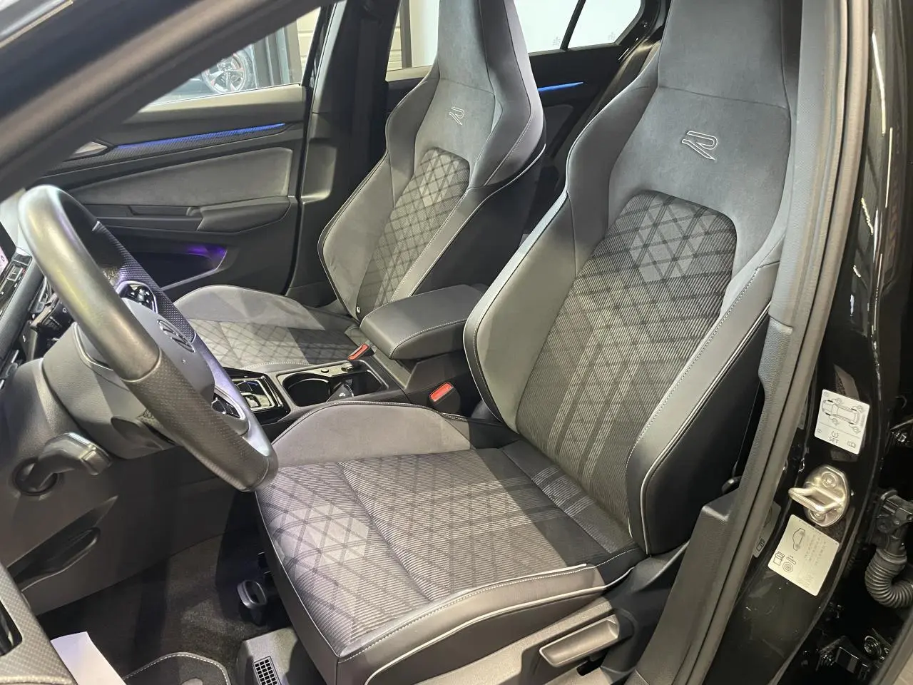 Vue intérieure côté conducteur de la Volkswagen Golf VIII R-Line Black avec sièges sport gris et détails carbone.