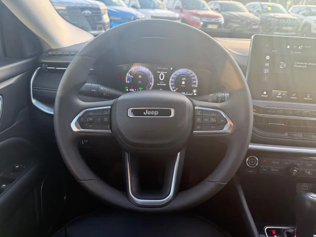 Vue intérieure centrée sur le volant Jeep du Compass 2024 avec tableau de bord numérique et écran tactile.