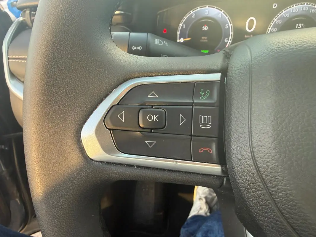 Gros plan sur les commandes gauche du volant du Jeep Compass bleu 2024 avec affichage numérique du tableau de bord.