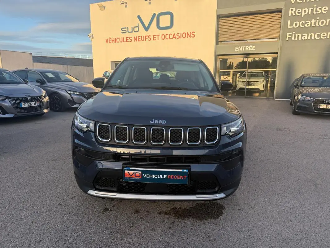 Vue de face d’un Jeep Compass bleu 2024 avec calandre distinctive et plaque « Véhicule récent » sur un parking extérieur.
