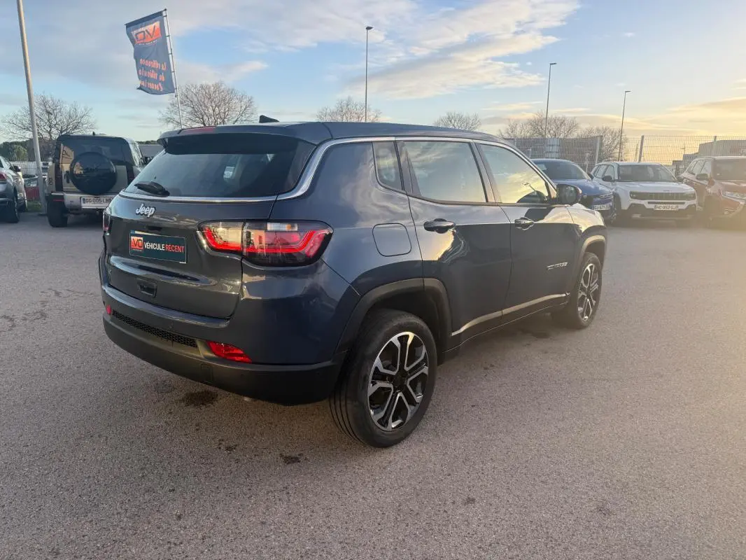 Vue 3/4 arrière droite du Jeep Compass bleu 2024 avec jantes alliage 18 pouces et feux arrière LED allumés.