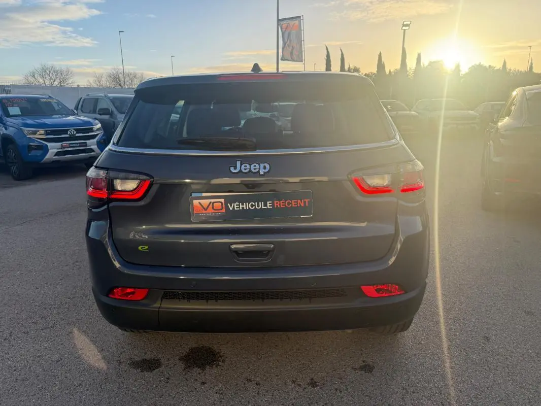Vue arrière d'un Jeep Compass bleu foncé 2024 avec feux LED allumés, sur parking extérieur en fin de journée.