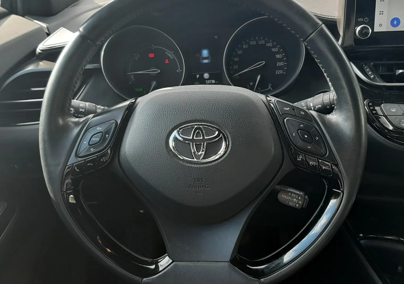 Vue intérieure centrée sur le volant noir du Toyota C-HR 1.8 Hybrid 2023 avec tableau de bord et écran tactile visibles.