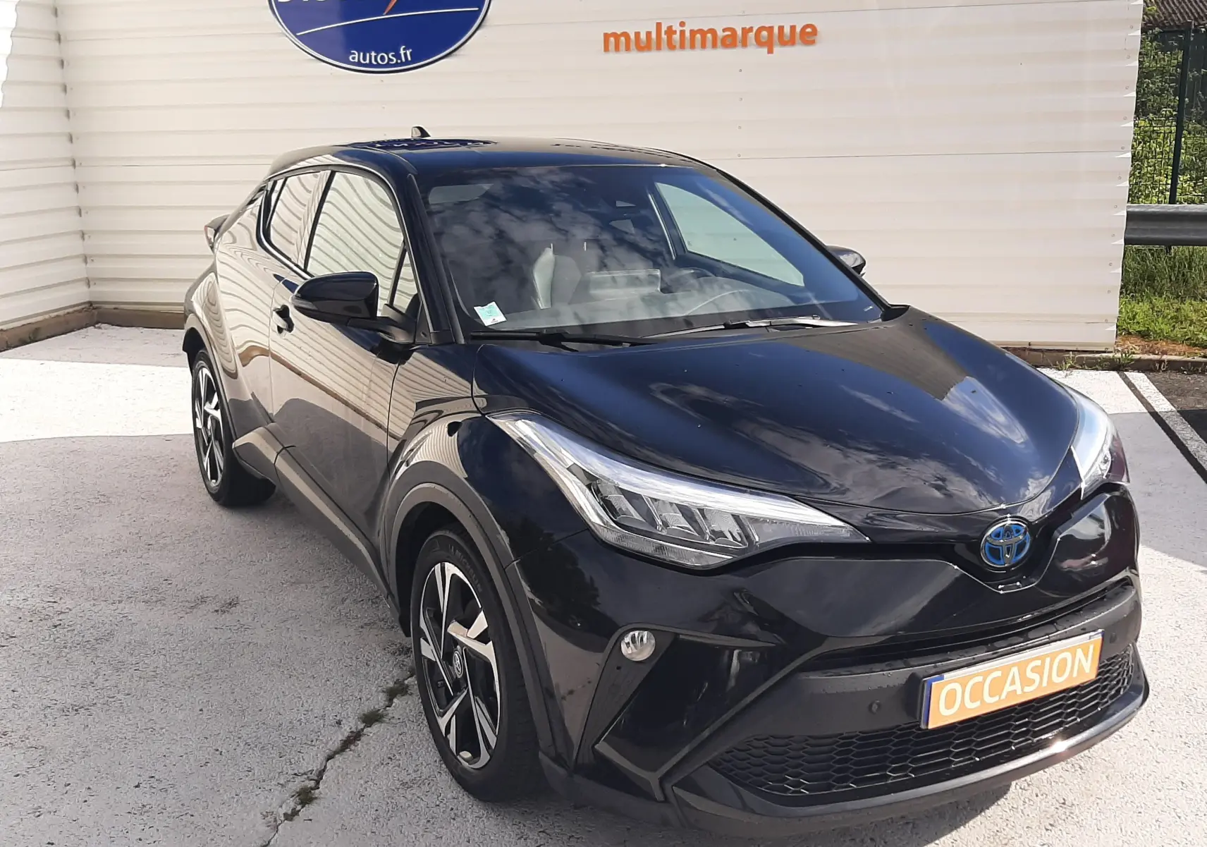 Vue 3/4 avant d'un Toyota C-HR 1.8 Hybrid noir 2023, avec jantes bi-ton et feux LED distinctifs.