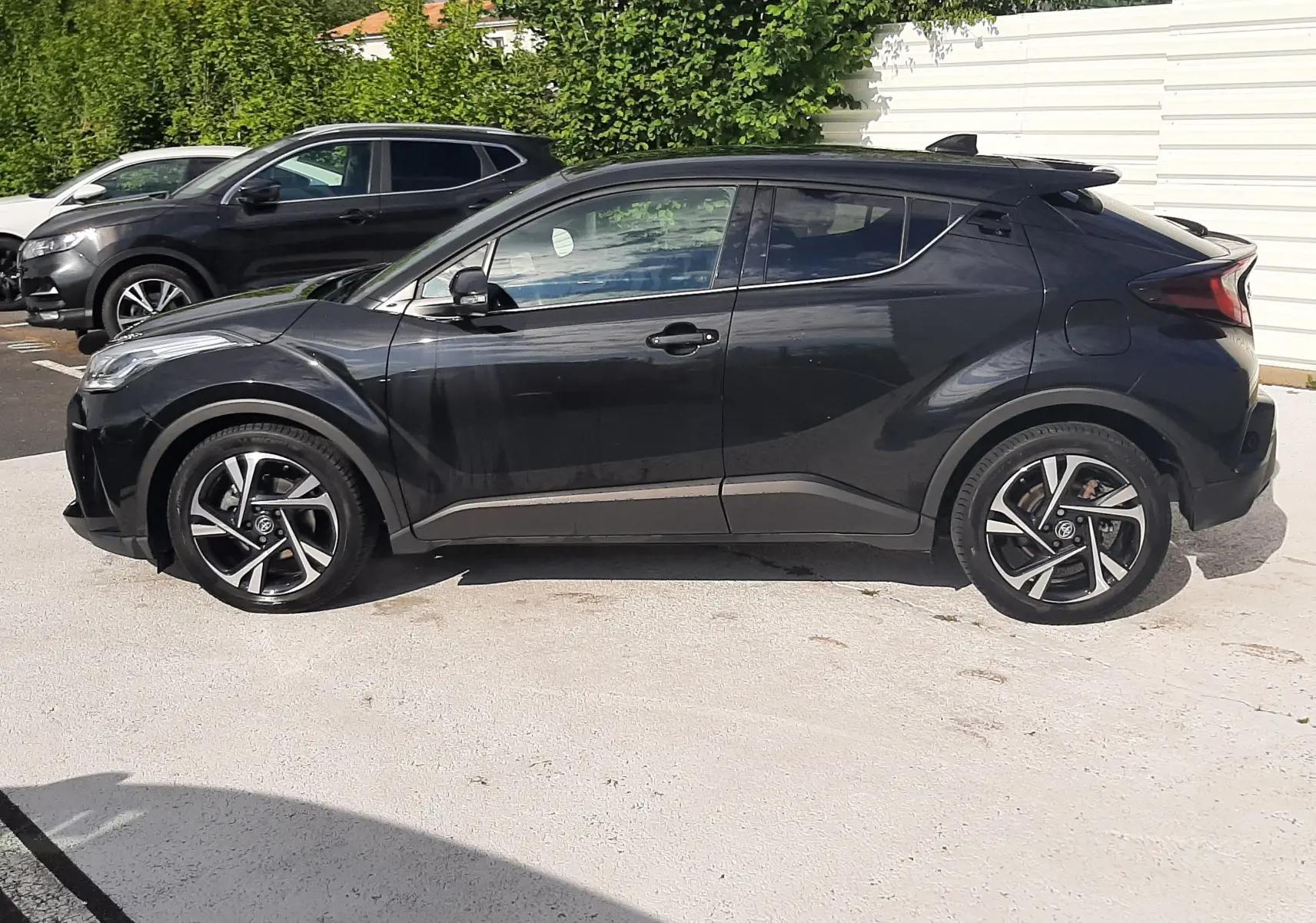 Toyota C-HR 1.8 Hybrid noir vu de profil côté gauche, avec jantes alliage bicolores et lignes sculptées.