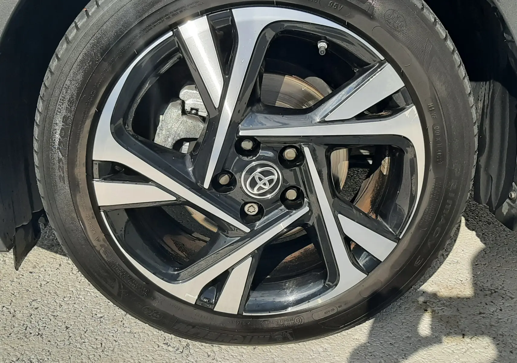 Gros plan sur la jante alliage bicolore noire et argentée du Toyota C-HR 1.8 Hybrid 2023 avec logo Toyota au centre.
