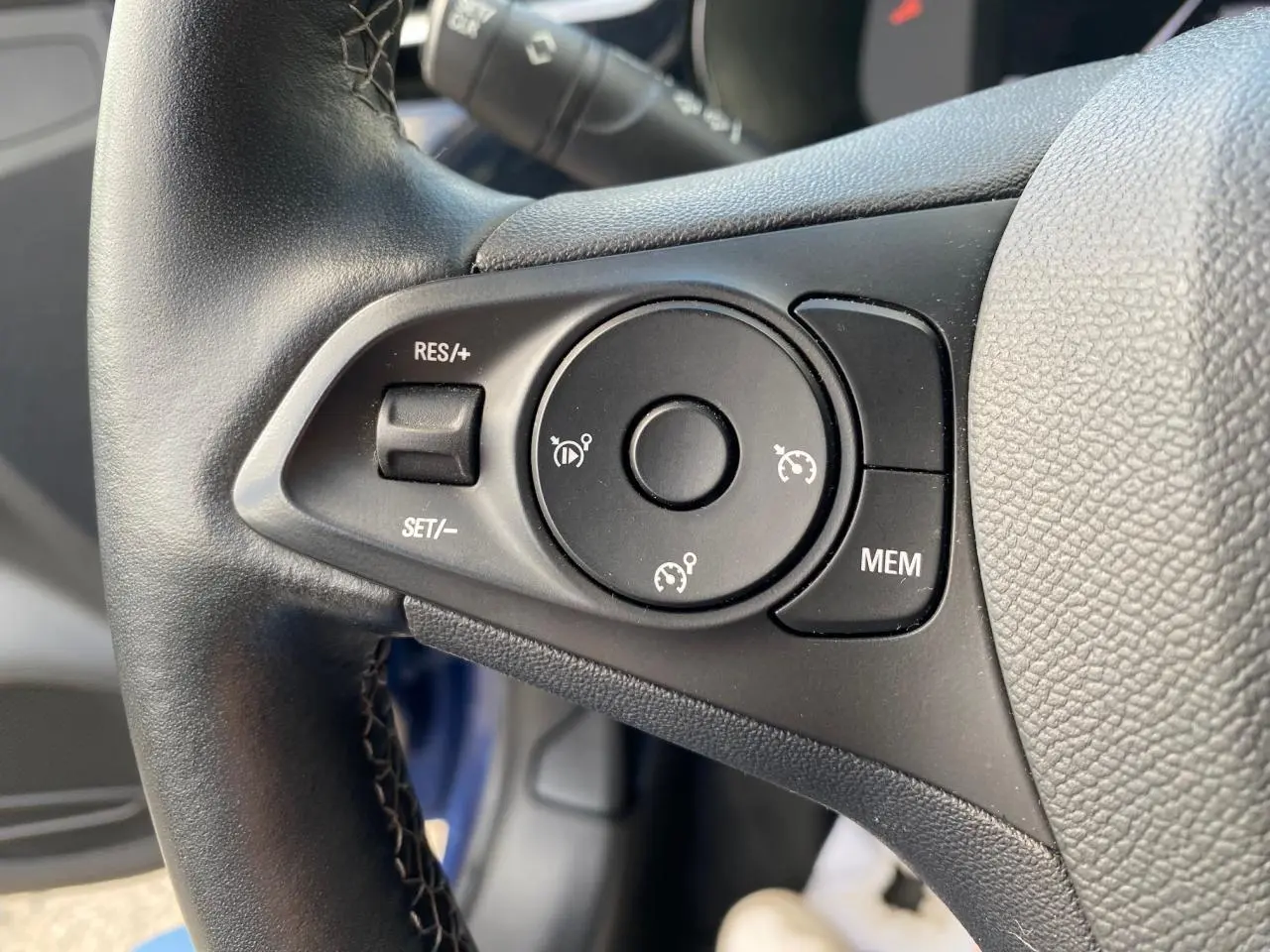 Gros plan sur les commandes du régulateur de vitesse au volant en cuir d'une Opel Corsa bleu nautique 2021.