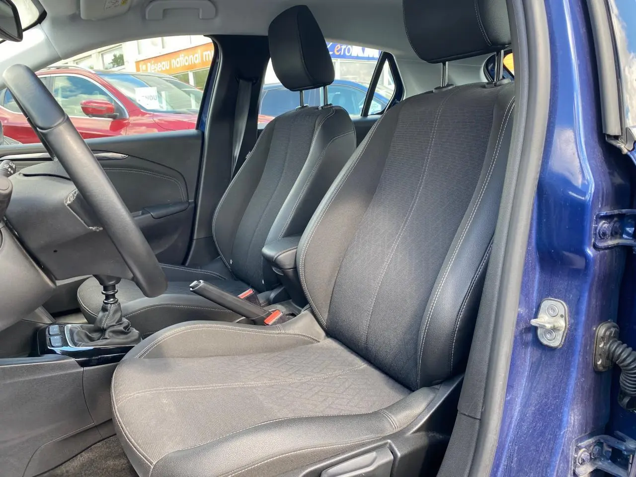 Vue intérieure côté conducteur de l’Opel Corsa bleu nautique, montrant les sièges avant et le levier de vitesse manuel.