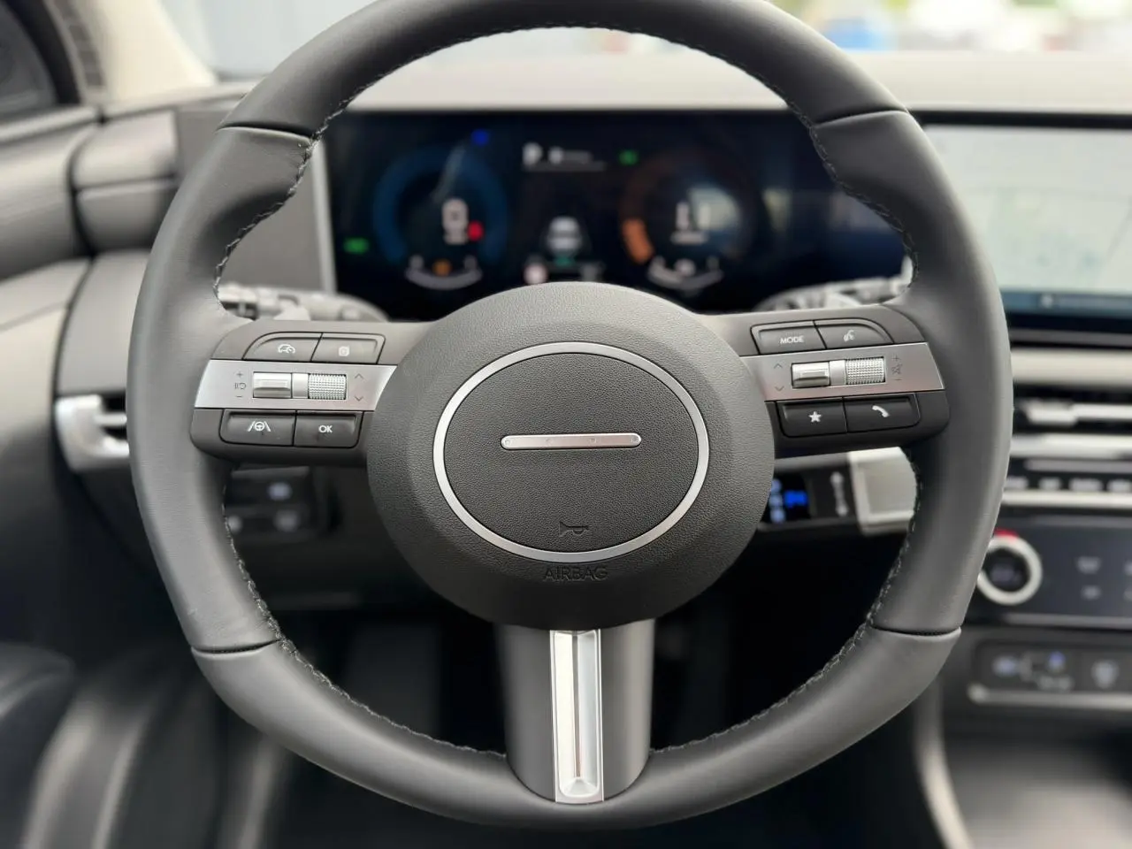 Vue rapprochée du volant noir du Hyundai Tucson 2026 avec commandes intégrées et tableau de bord numérique flou en arrière-plan.