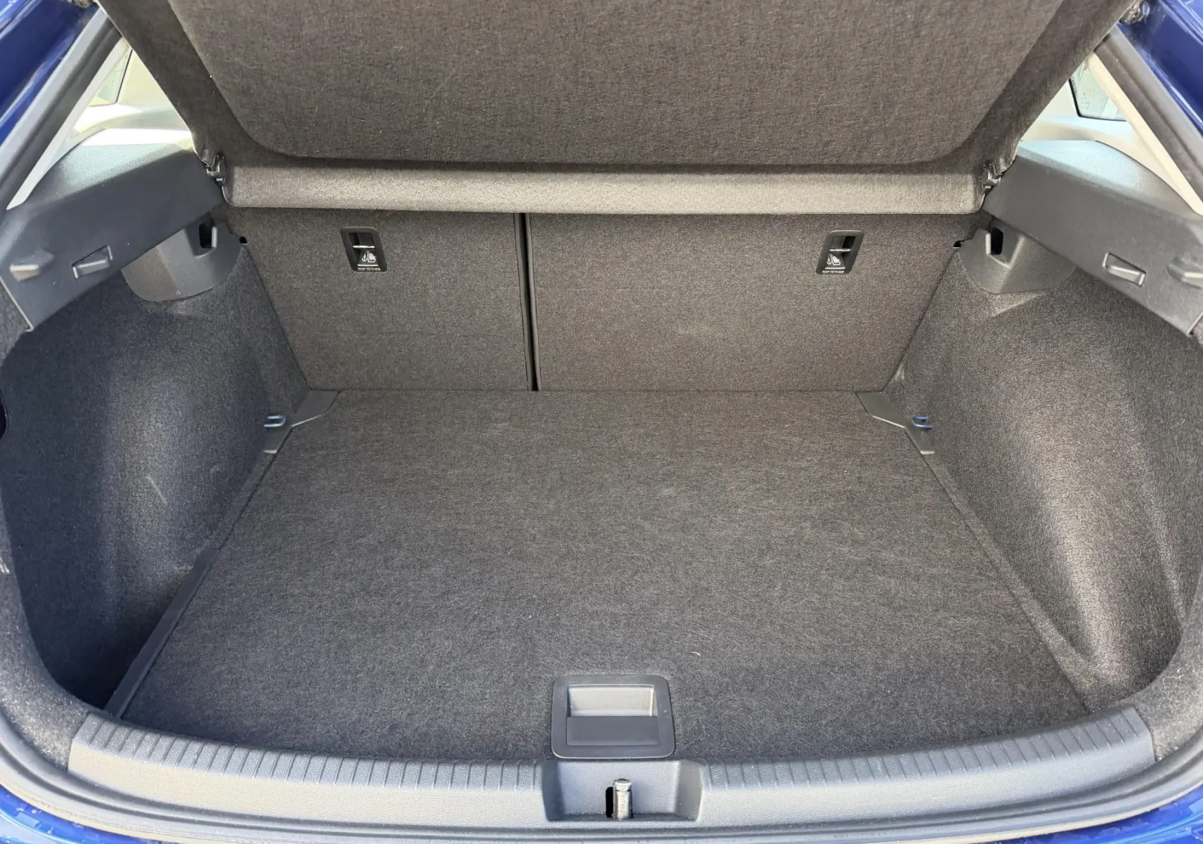Coffre ouvert du Volkswagen Taigo bleu, vue arrière montrant l'espace de chargement et le plancher réglable.