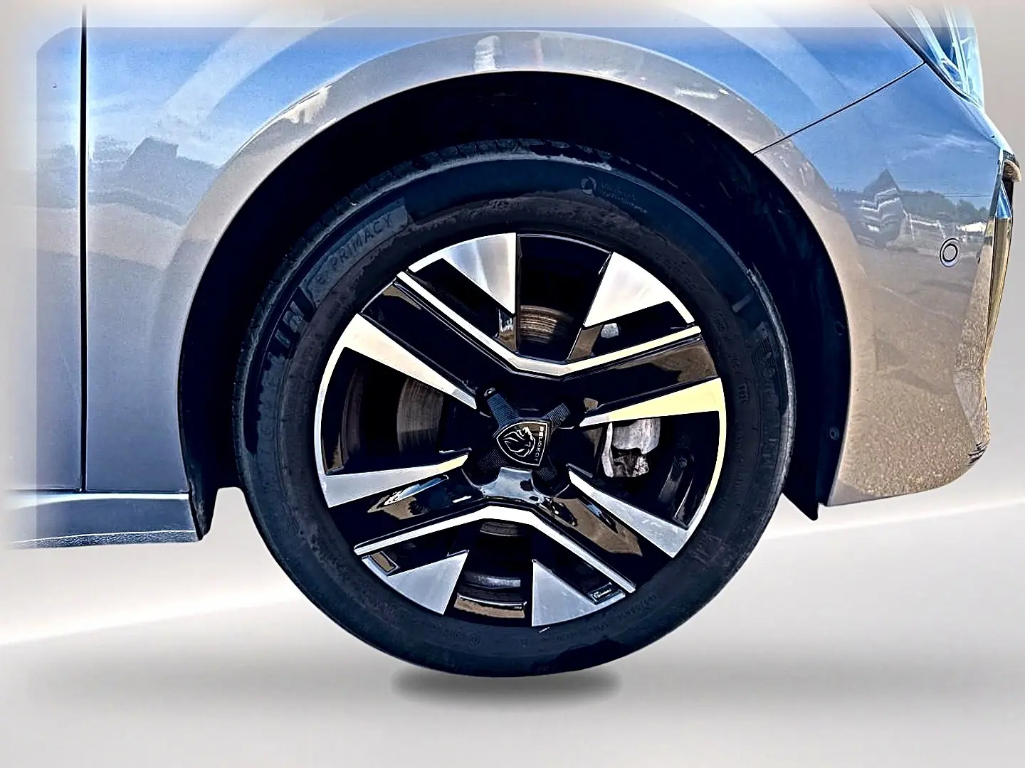 Gros plan sur la roue avant droite d’une Peugeot 208 1.2 100 Allure gris Artense avec jante alu bicolore.