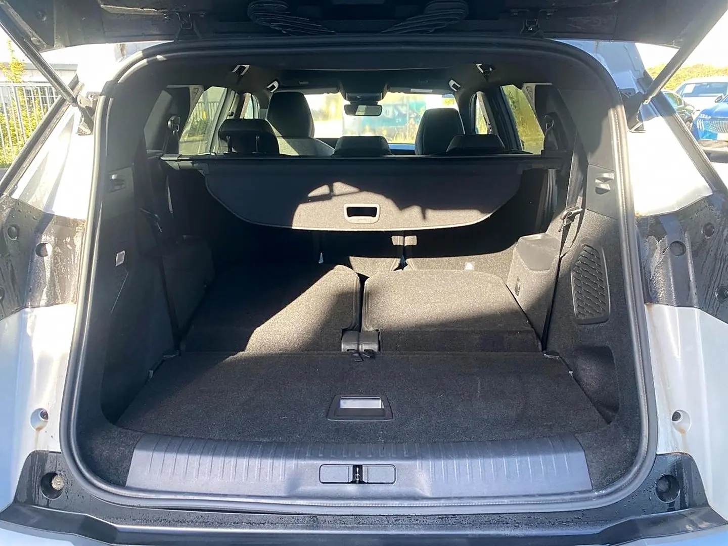 Coffre ouvert vu de l'arrière d'un Peugeot 5008 blanc avec banquette arrière rabattue et cache-bagages déployé.