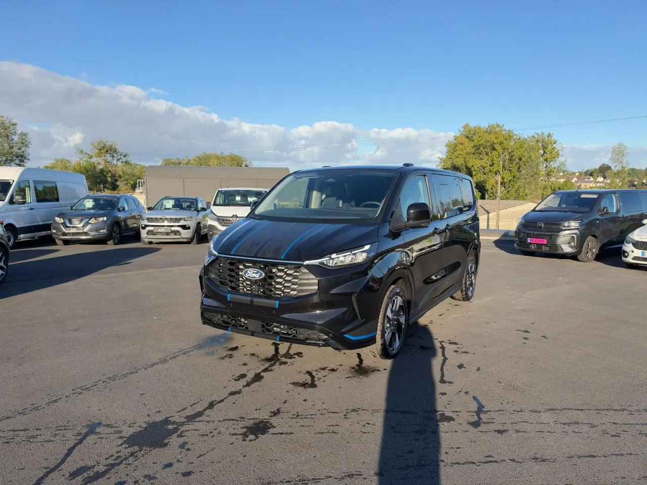 Ford Transit Fourgon Custom noir vu de 3/4 avant droit sur un parking en extérieur, avec jantes alliage sport.