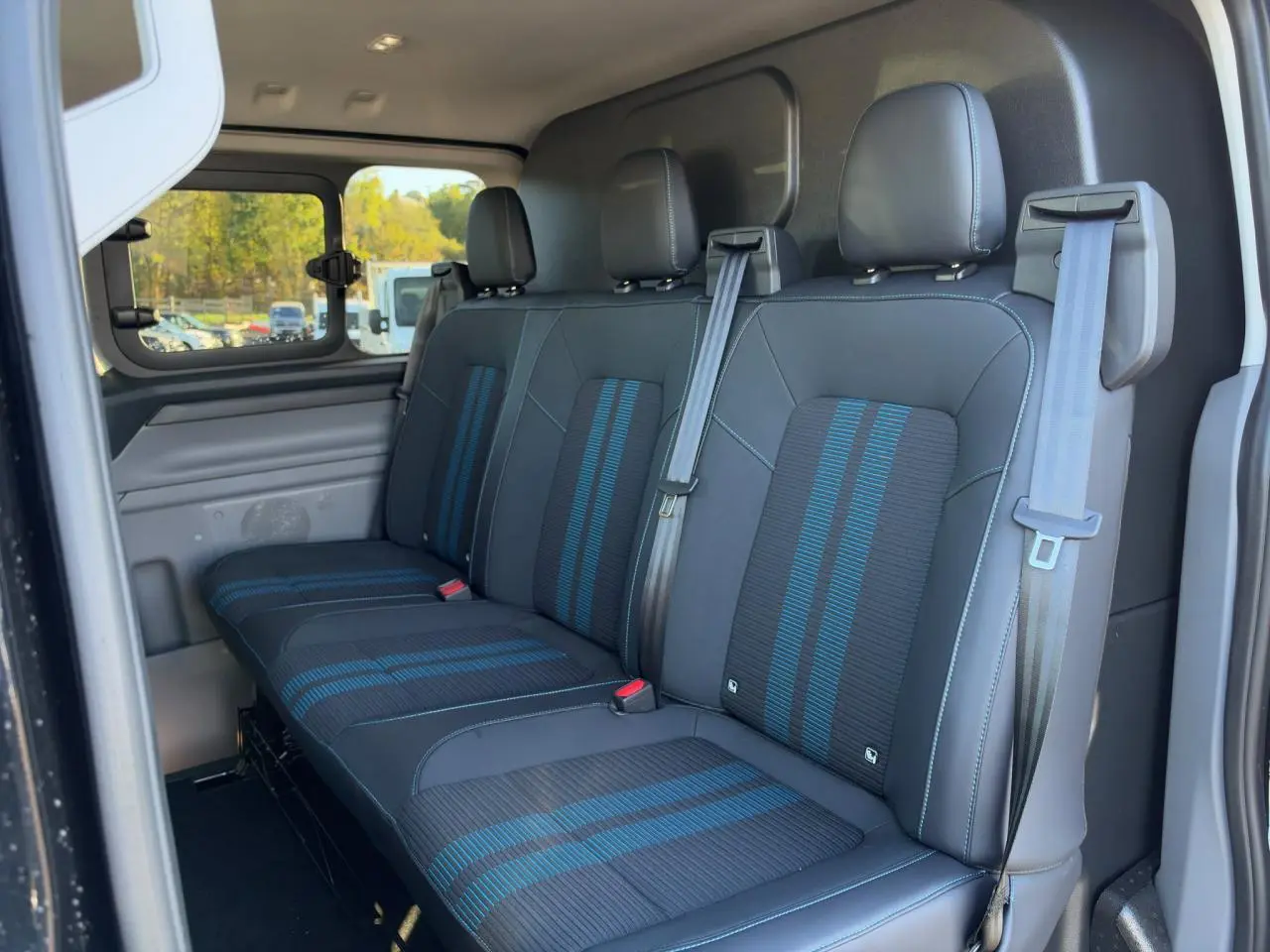 Vue intérieure côté droit du Ford Transit Fourgon 2026, banquette arrière noire avec bandes bleues et ceintures grises.