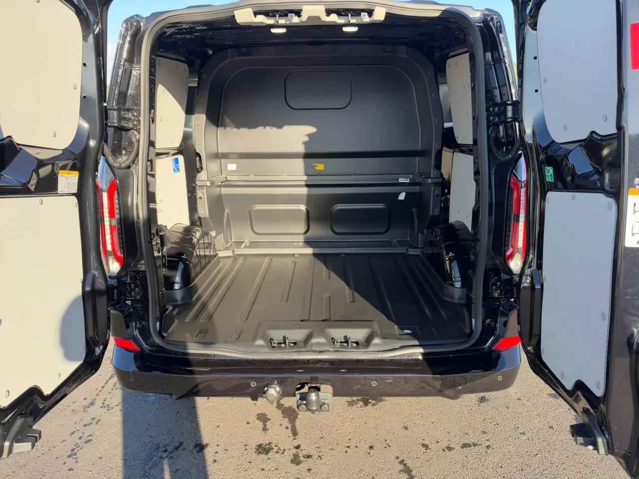 Vue arrière du Ford Transit Fourgon noir 2026 avec portes ouvertes et espace de chargement vide, crochet d'attelage visible.