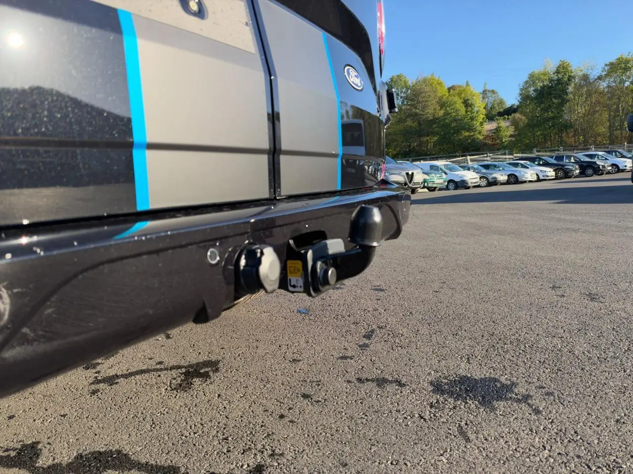 Gros plan sur le crochet d'attelage arrière du Ford Transit Fourgon noir avec bandes bleues, sous un ciel dégagé.