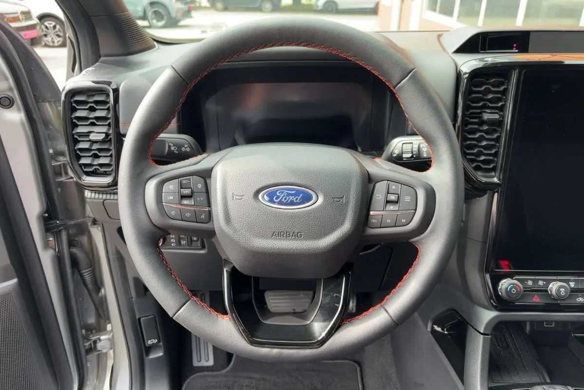 Vue rapprochée du volant cuir noir avec surpiqûres rouges du Ford Ranger Wildtrak Plus 2026 gris iconic, tableau de bord moderne.