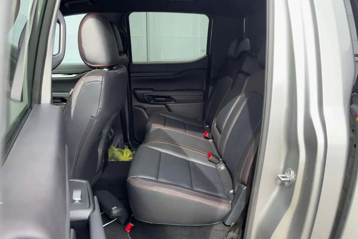 Vue latérale droite sur l'intérieur arrière du Ford Ranger Wildtrak gris iconic avec sièges cuir noirs et surpiqûres orange.