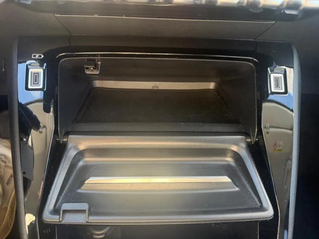 Vue rapprochée de la console centrale noire du Peugeot 208 Hybrid 110 e-DCS6 Allure 2024 avec compartiment ouvert.