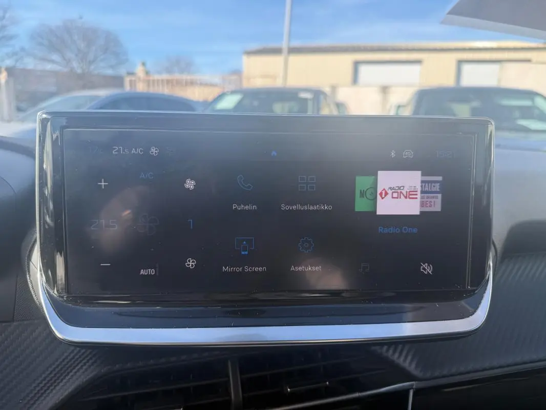 Écran tactile central de la Peugeot 208 Hybrid blanc, affichant les commandes climatisation et radio, vue intérieure frontale.