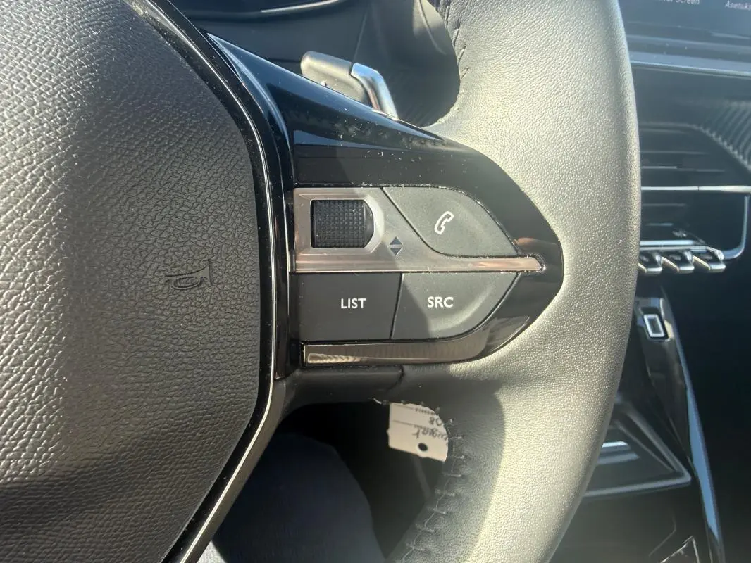 Gros plan sur les commandes gauche du volant noir de la Peugeot 208 Hybrid 110 e-DCS6 Allure 2024, avec boutons LIST et SRC.