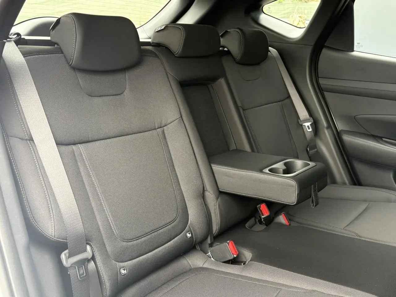 Vue intérieure sur les sièges arrière noirs du Hyundai Tucson 2026 avec accoudoir central et ceintures visibles.