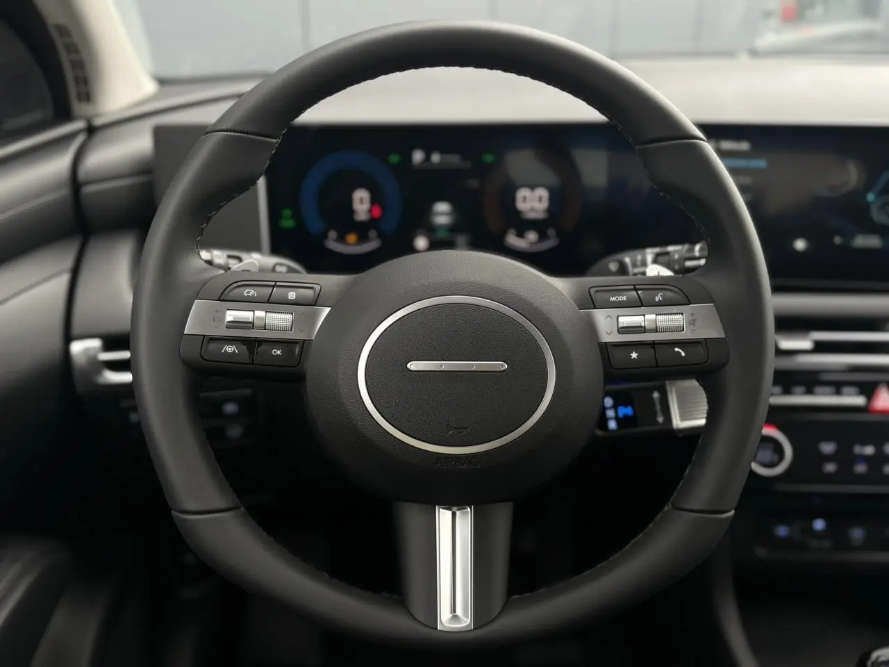 Gros plan sur le volant noir multifonction du Hyundai Tucson 2026 avec tableau de bord numérique en arrière-plan flou.